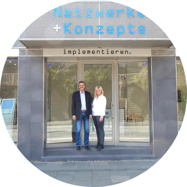 Kreis gefüllt mit dem Bild von Netzwerke + Konzepte - vor der Tür stehend die Inhaber Andre und Dagmar Schneider