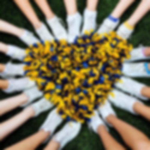 Viele Füße, die zusammen ein Herz. Das Herz wird mit geld blauen Pompons ausgefüllt.