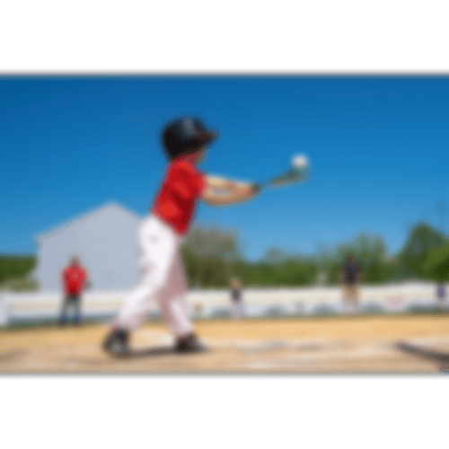 Kind in Baseballoutfit und Baseballschläger in der Hand, mit welchem er zum Schlag ausholt.