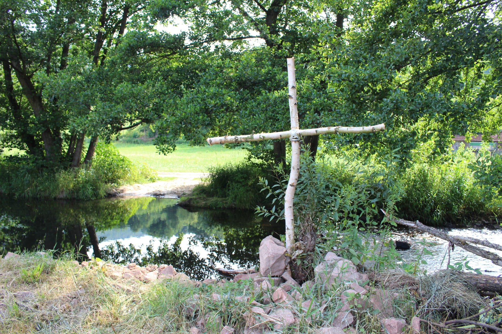 Kreuz gefertigt aus Birkenstämmen, dass vor einem Fluss steht