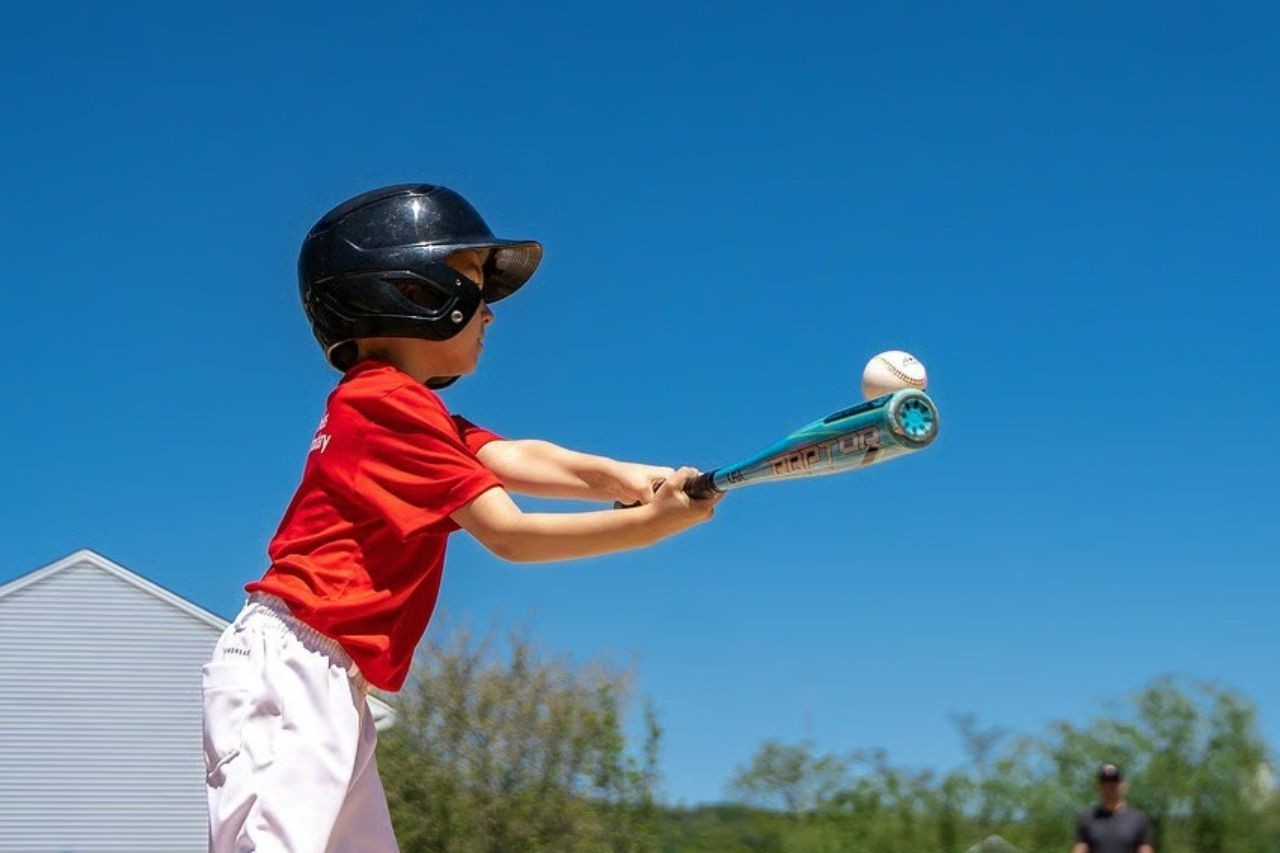 Kind in Baseballoutfit und Baseballschläger in der Hand, mit welchem er zum Schlag ausholt.